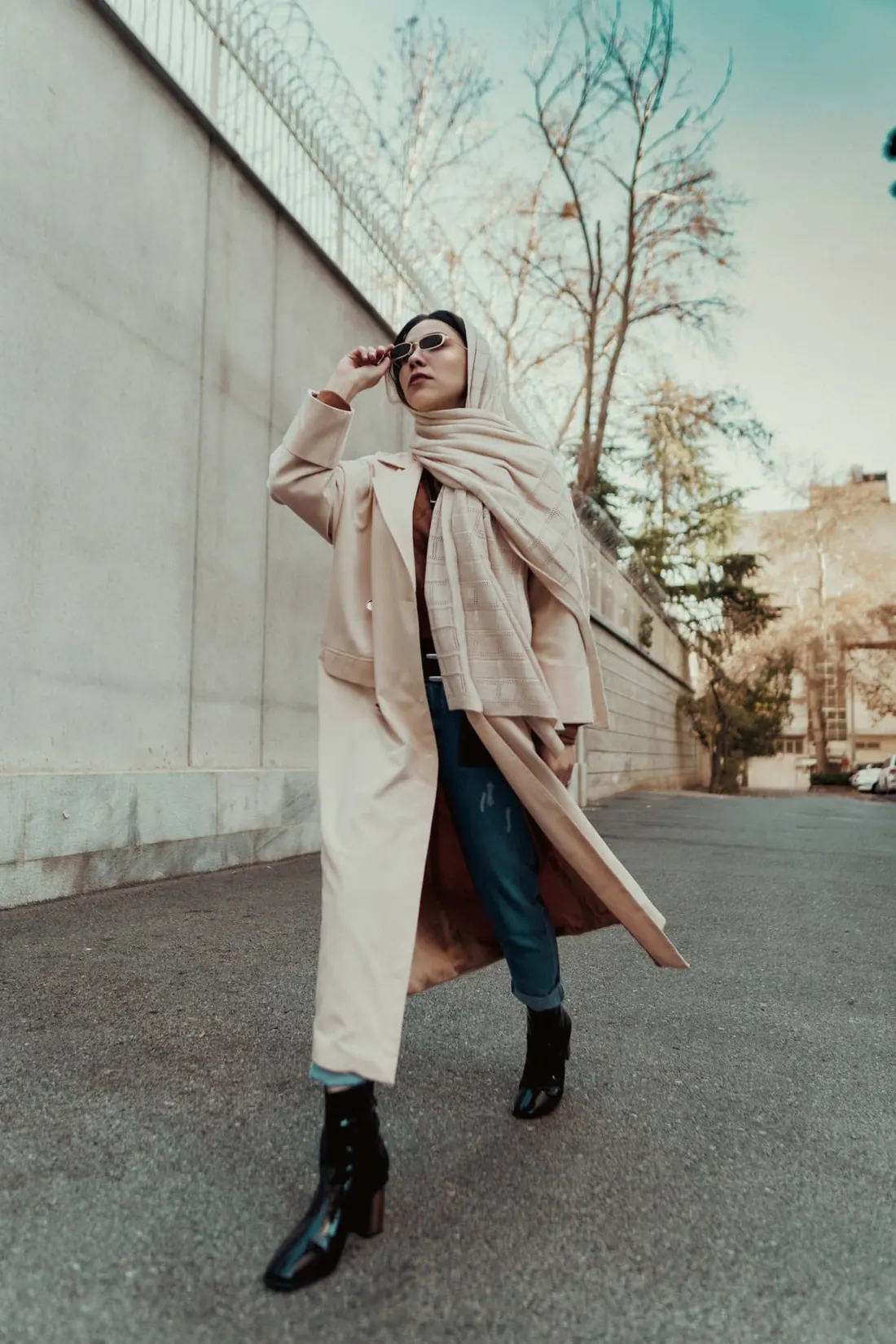 A woman in a long cream coat walking past a concrete wall