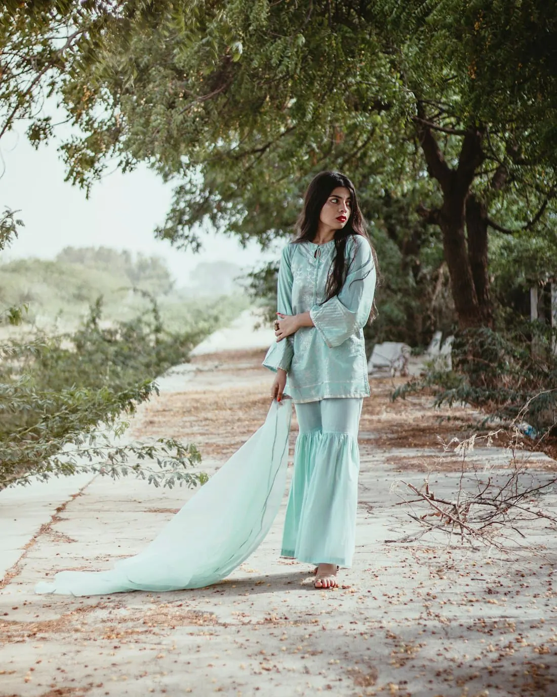 A woman in a mint sharara set on a tree-lined path