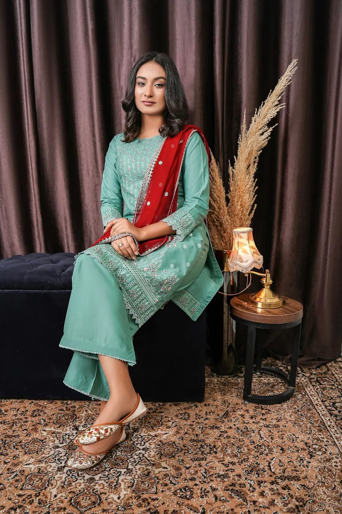 A woman in a teal silk kurta set seated with a red dupatta
