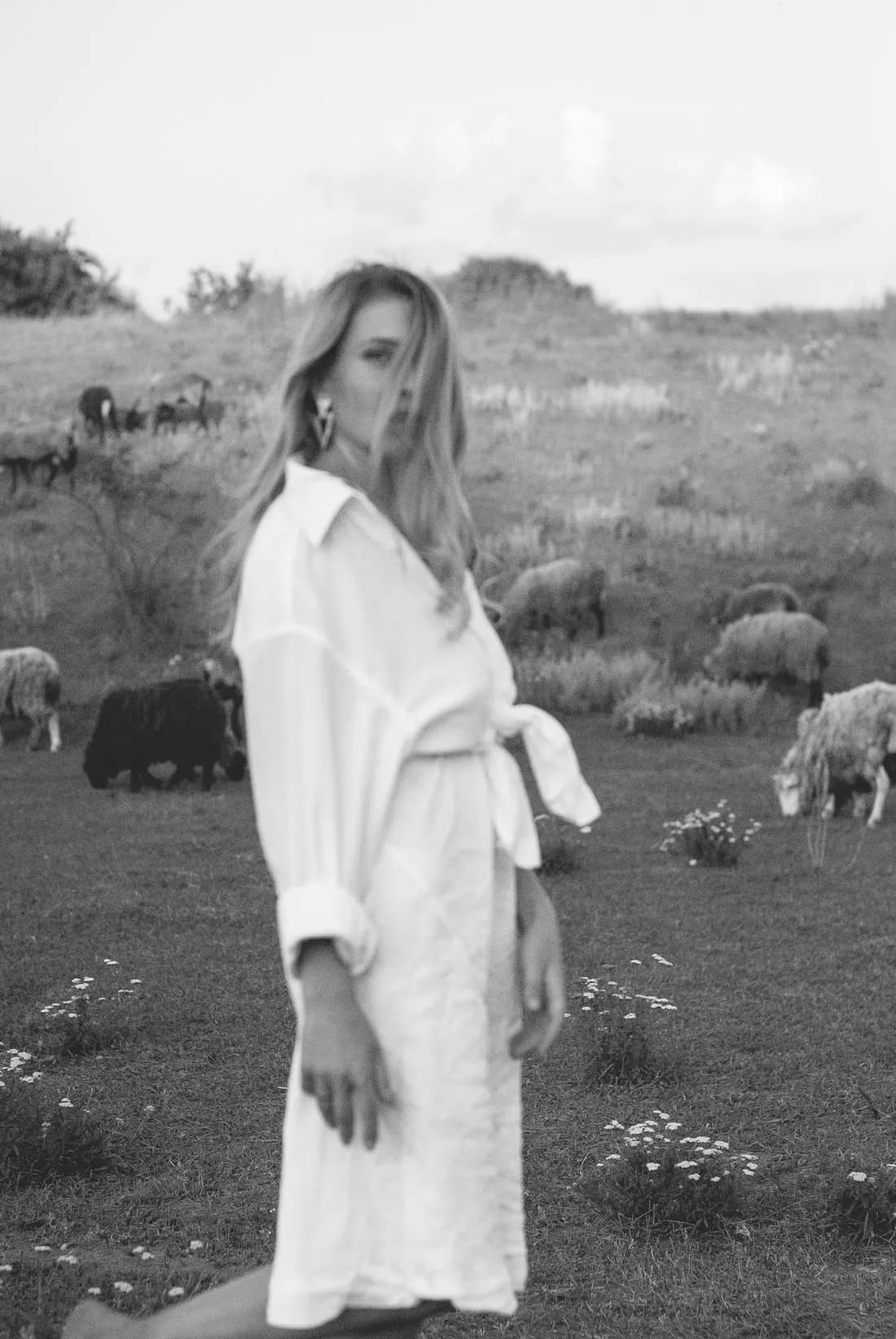 Black and white portrait of a woman in a long white shirt dress, standing in a field
